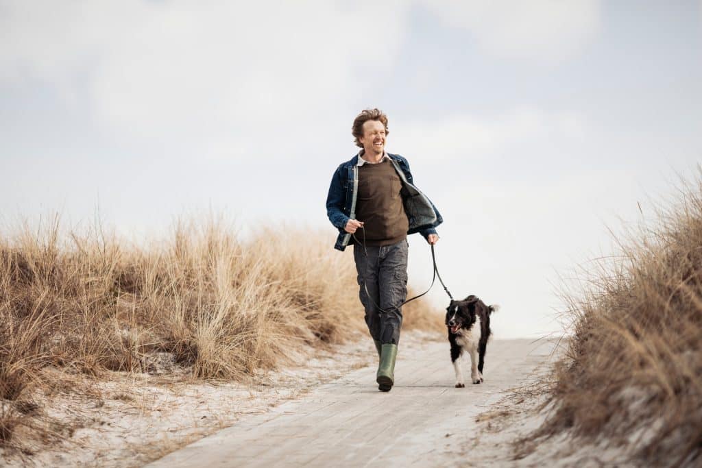 Mann mit Hund in der Natur: Ein aktiver Lebensstil kann das Risiko für Symptome einer vergrößerten Prostata reduzieren.