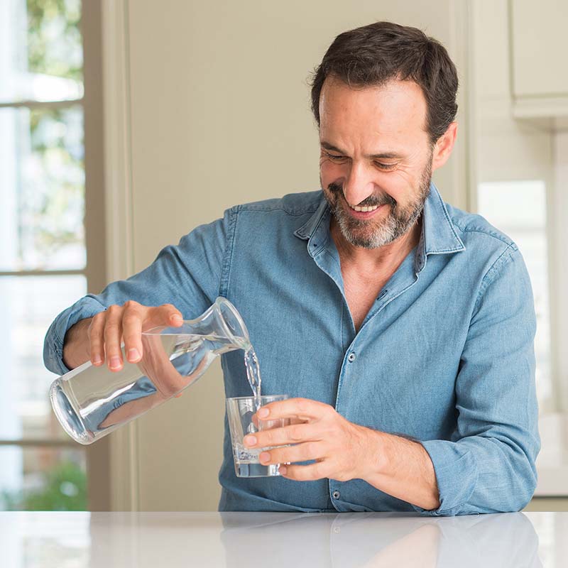 Mann schenkt sich ein Glas Wasser ein, um Prostatamittel einzunehmen.