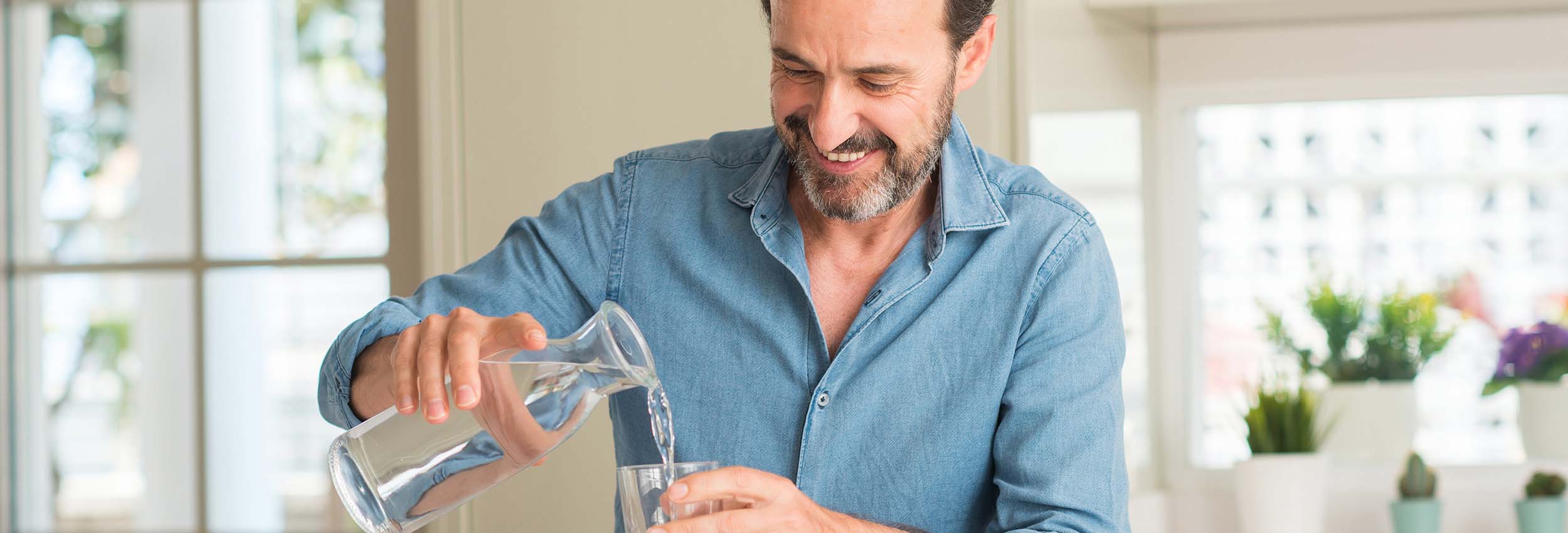 Mann schenkt sich ein Glas Wasser ein, um Prostatamittel einzunehmen.