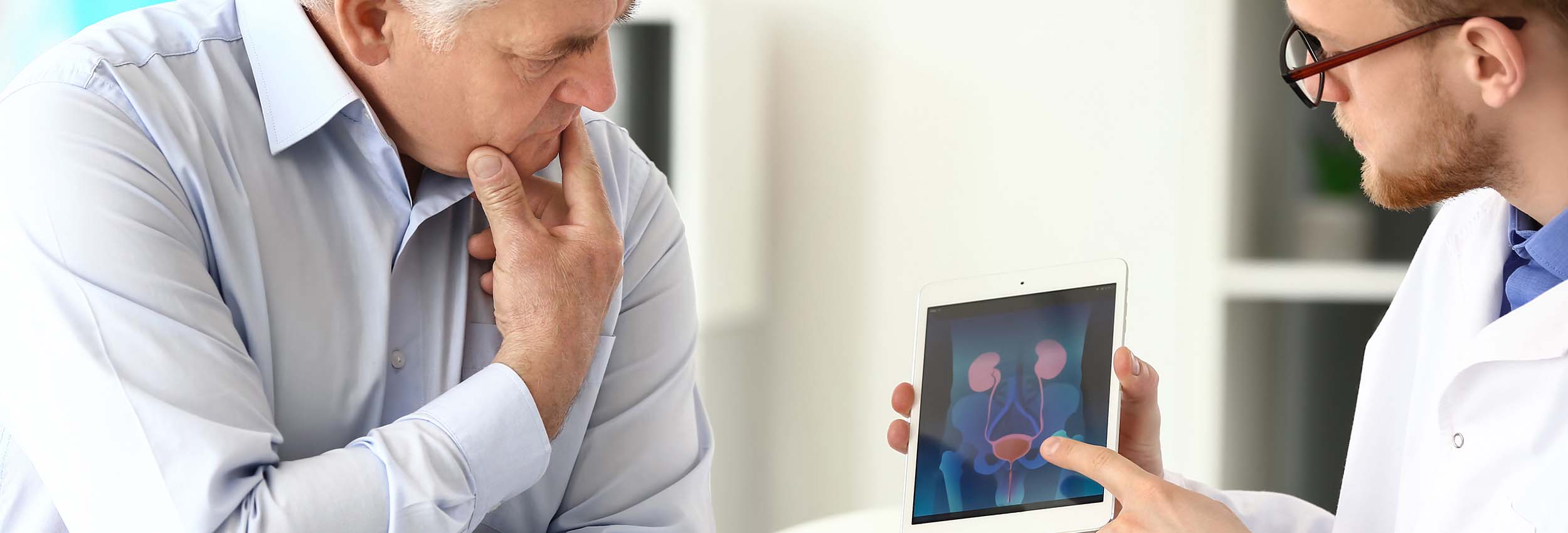 Mediziner erklärt einem Patienten anhand einer Darstellung auf dem Tablet seine Prostatabeschwerden.